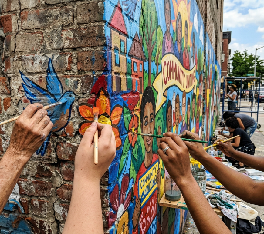 Artists painting a colorful community mural on a brick wall
