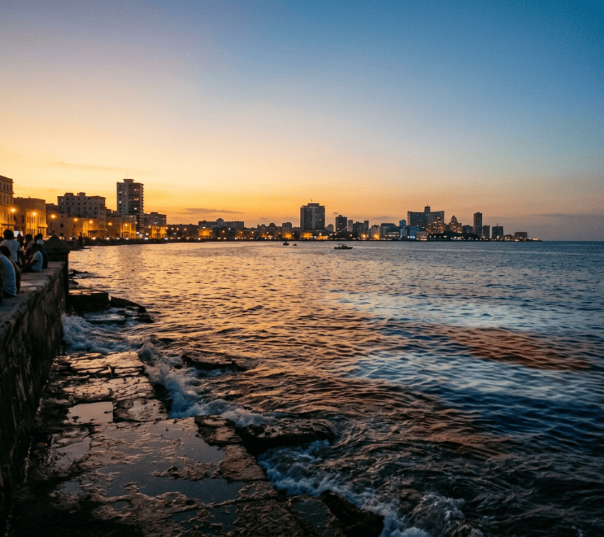 People on a seawall overlooking Havana’s illuminated waterfront at sunset
